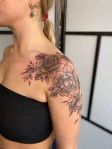 Sort blomstertatovering på skulder og overarm