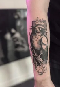 Sort fugletatovering med krone på underarm