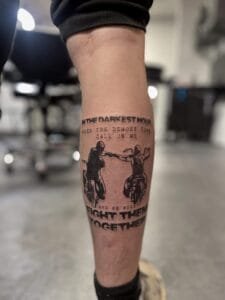 Tatovering af to cyklister og citat på ben