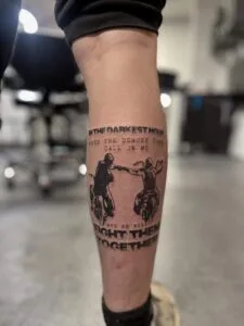 Tatovering af to cyklister og citat på ben