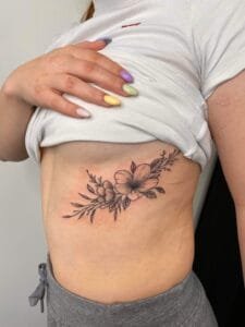Blomster tatovering på ribben under hvid t-shirt