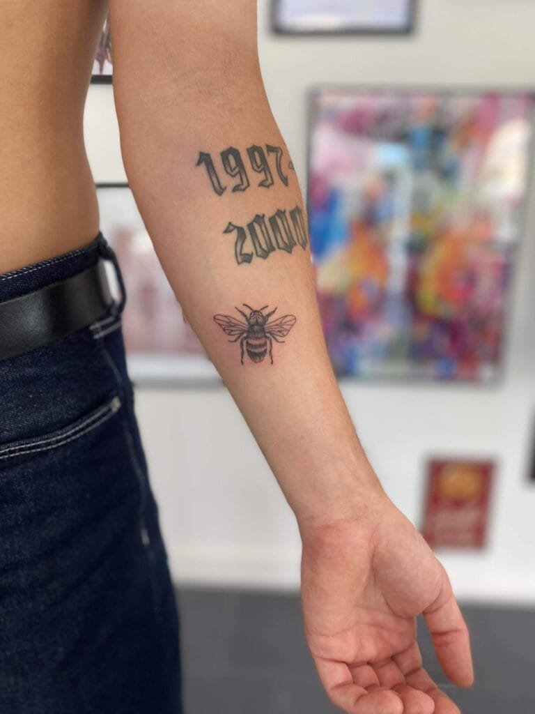 Arm med tatoveringer af årstal og bi