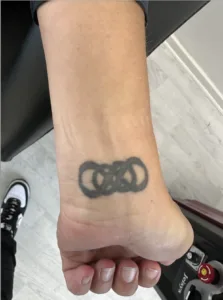 Sort tatovering med sammenflettede cirkler på håndled